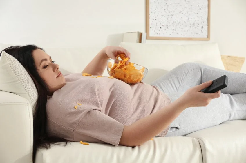 lazy overweight woman with chips watching tv on sofa at home