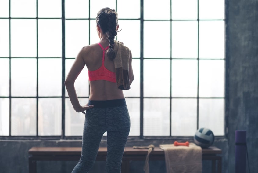 rear view of woman holding towel looking out window in loft gym
